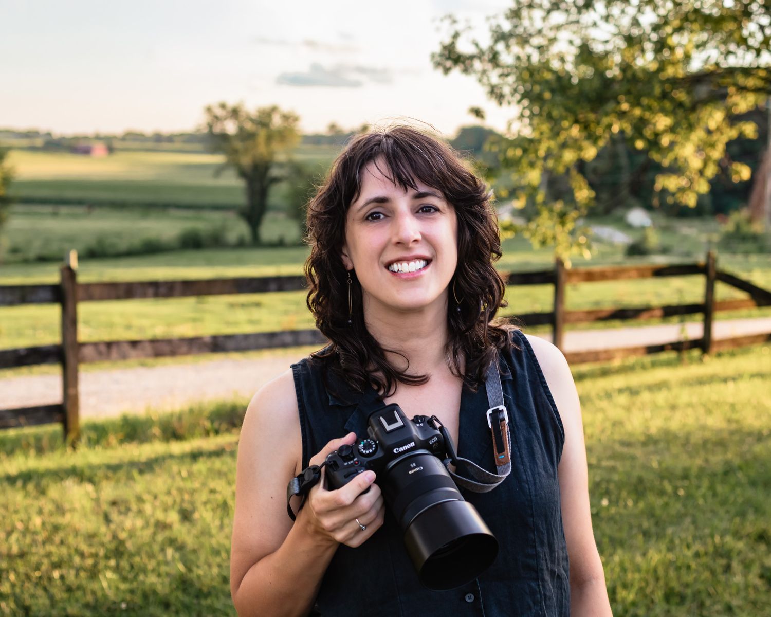 Self-portrait of Maryland family photographer Joanna Nolting outdoors at a farm, holding her camera.