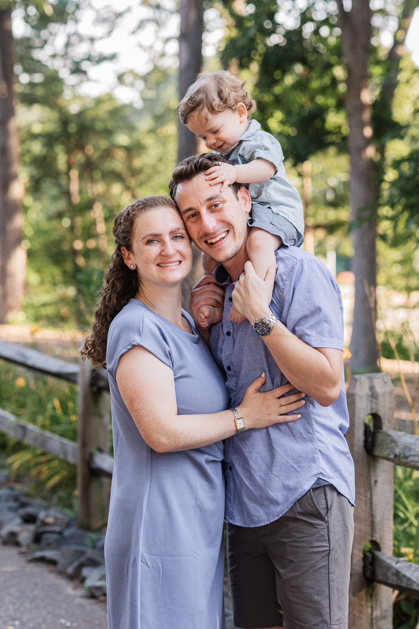 Parents standing together at a sunny park with their toddler on dad's shoulders