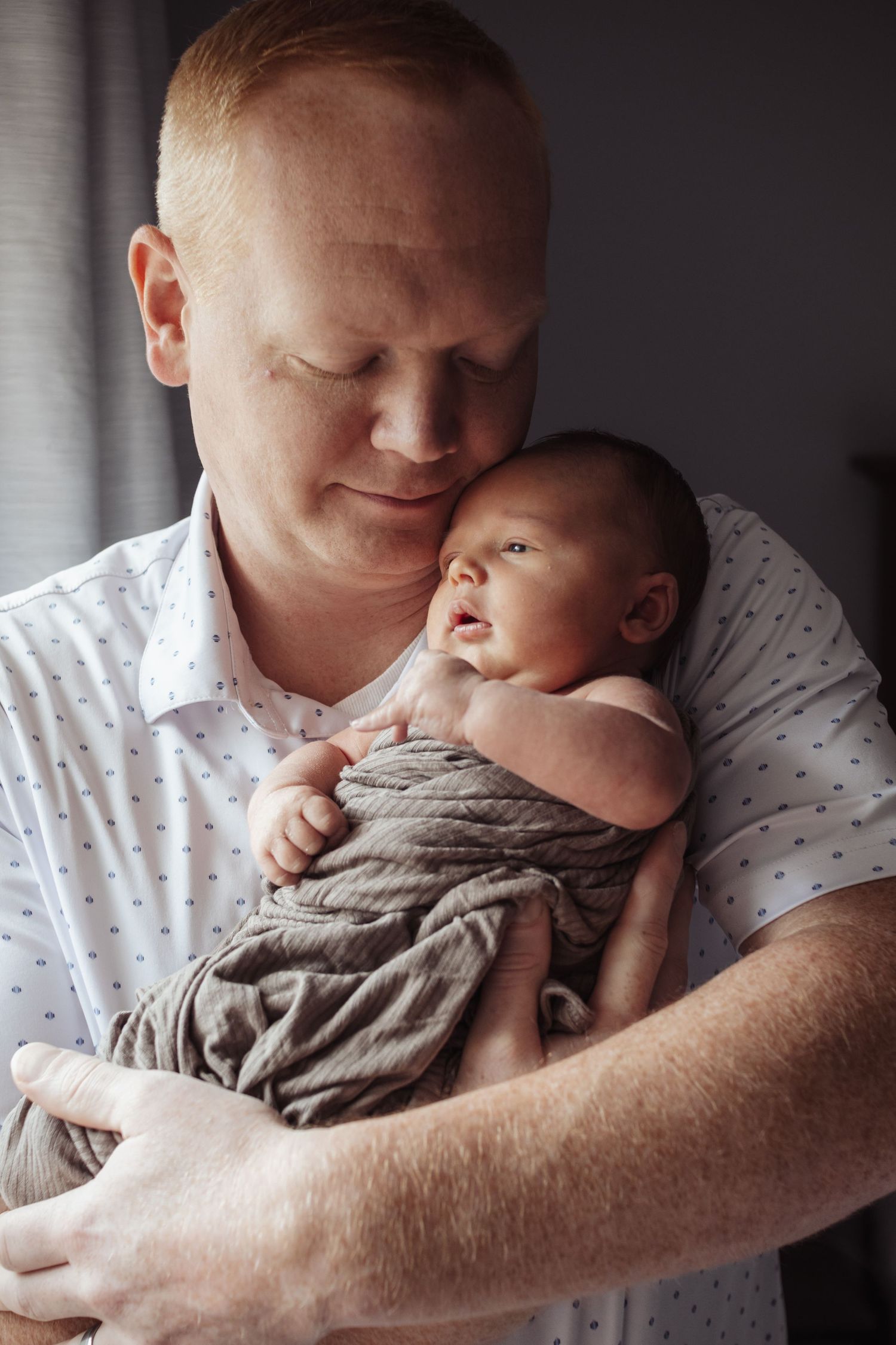 Father holding baby near a sunlit window during an in-home newborn lifestyle family photography session in Crofton, Maryland