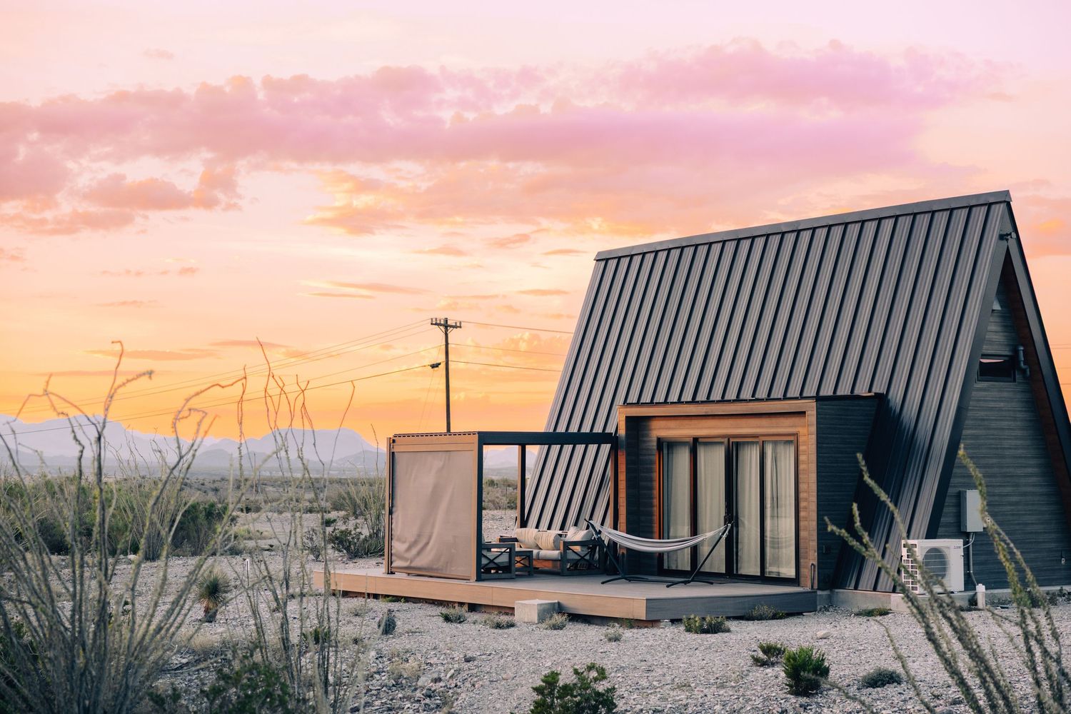 Modern A-frame cabins nestled in a desert landscape with dramatic sunsets and mountains in the background.