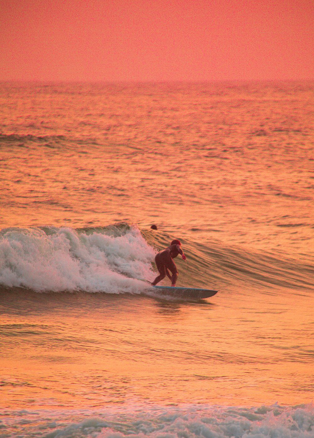 Surfer rides a wave during golden sunset with orange sky reflecting on the ocean waters.