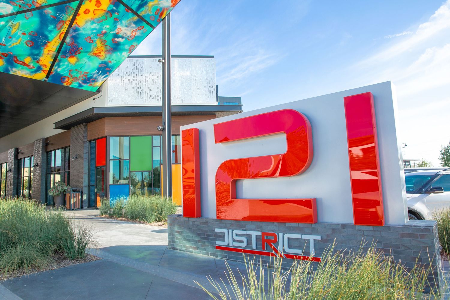 Colorful District 121 sign with red lettering at a modern commercial building entrance under a blue sky.