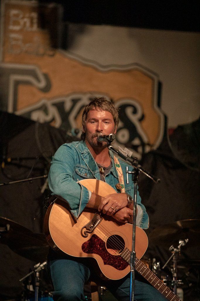 A musician in a turquoise shirt performs with an acoustic guitar on stage during a live performance.