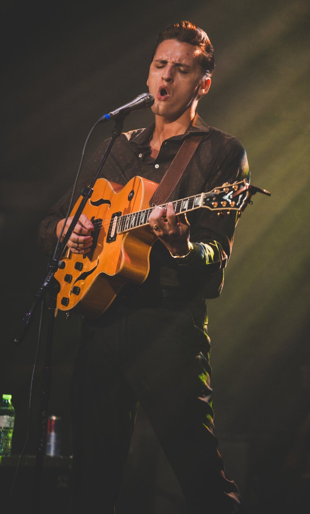 Musician from Red Clay Strays in dark attire plays orange guitar while singing into microphone on dimly lit stage.