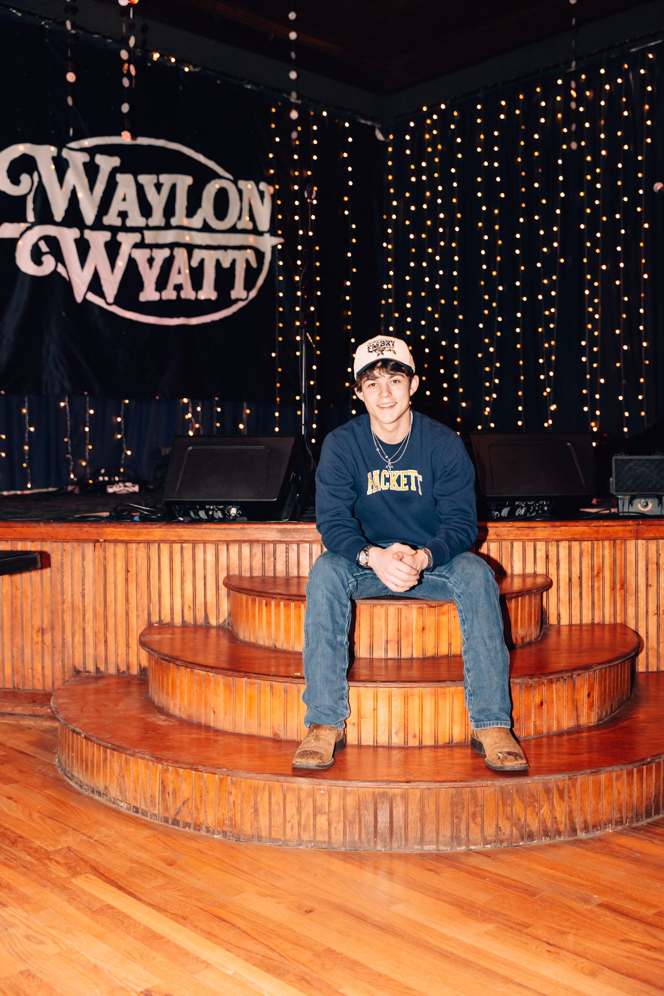 Interior of Waylon & Wyatt venue with wooden stage risers and twinkle lights backdrop displaying illuminated venue sign.
