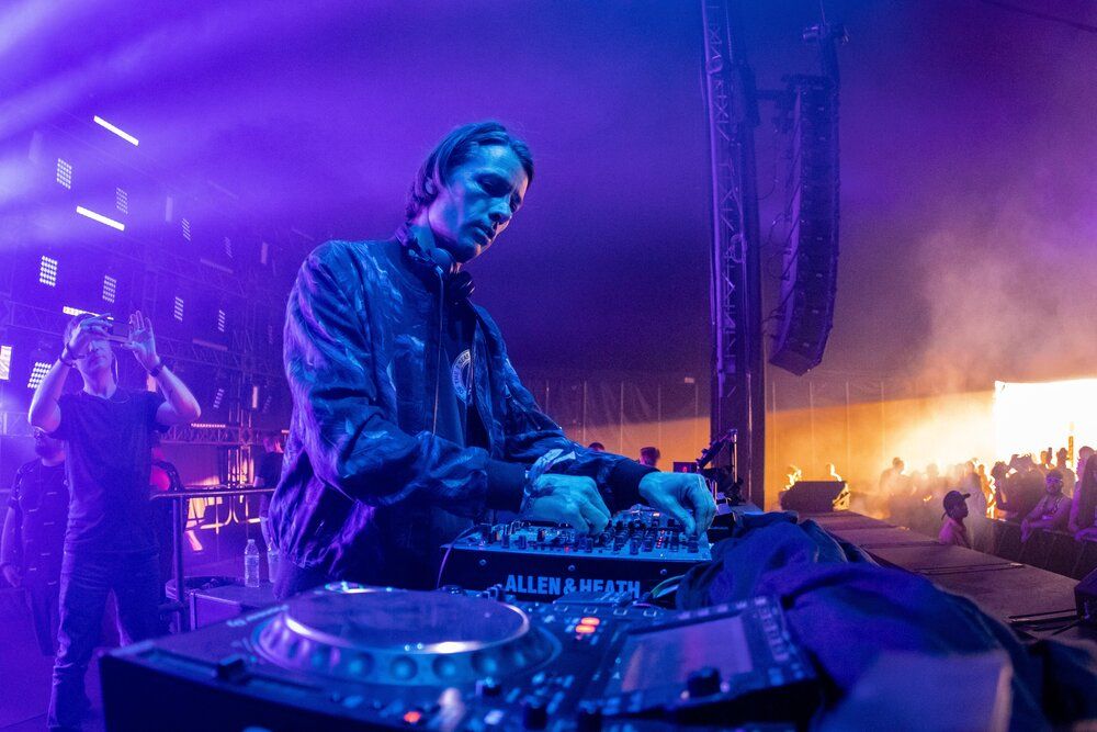 DJ mixing music on turntables under dramatic purple stage lighting at nightclub event.