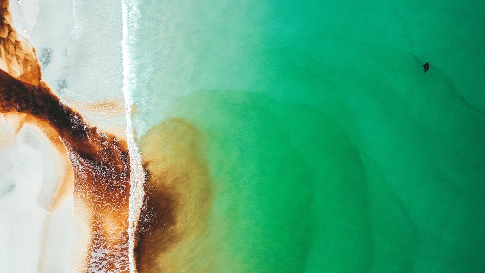 Aerial view of turquoise ocean waters meeting sandy beach with abstract patterns.