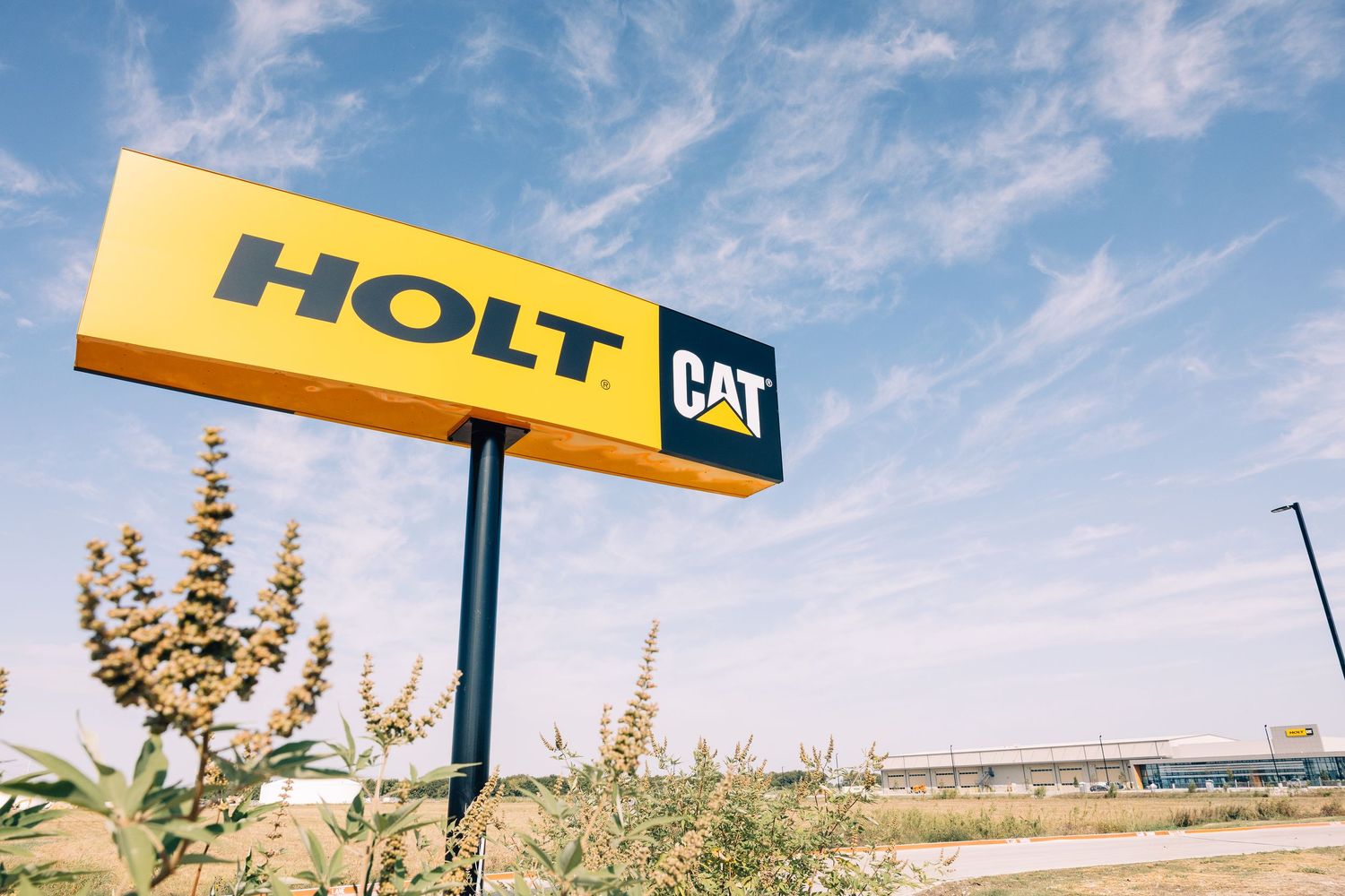 Holt CAT dealership sign against a blue sky, showcasing the yellow and black Caterpillar branding logo.