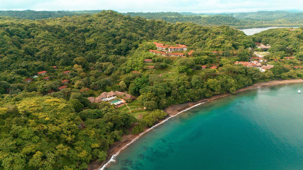 Aerial view of luxury villas nestled in lush jungle overlooking turquoise waters along Costa Rica's tropical coastline.