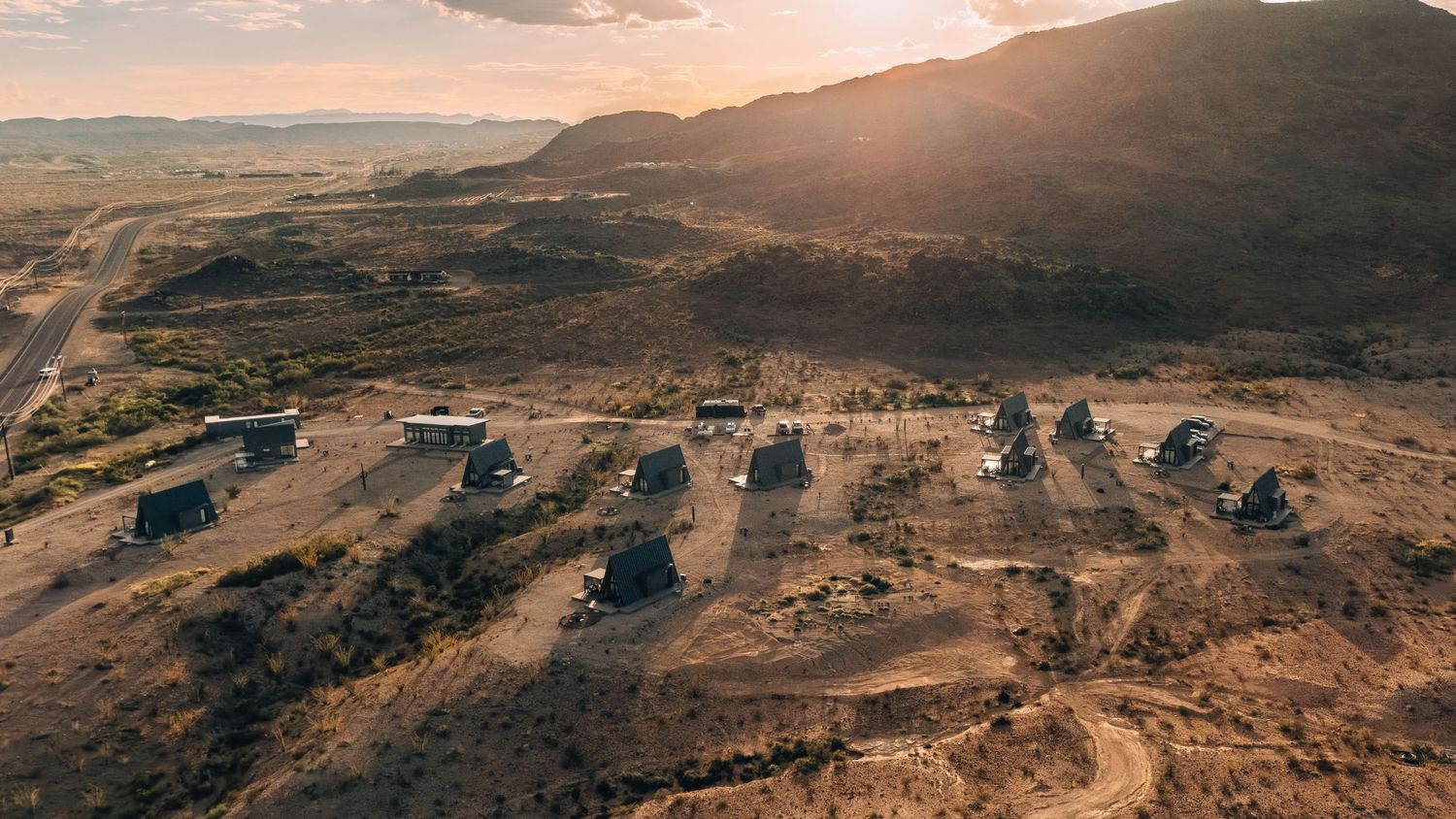A panoramic landscape of rolling desert hills and mountains bathed in warm golden sunlight at sunset.