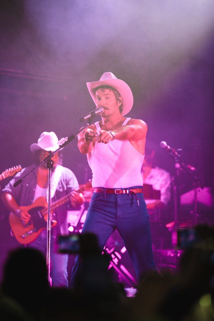 Country performer from Midland in white tank top and cowboy hat singing on stage with purple lighting.