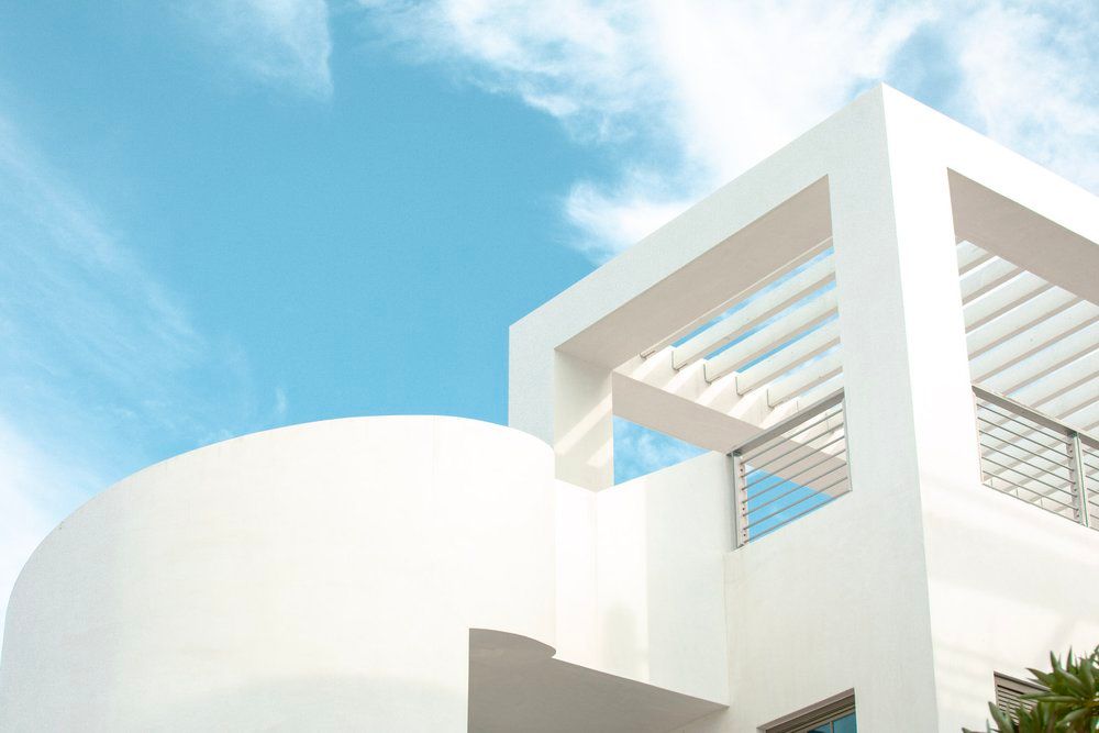 Modern white architectural building with curved walls and pergola against bright blue sky and sunlight.
