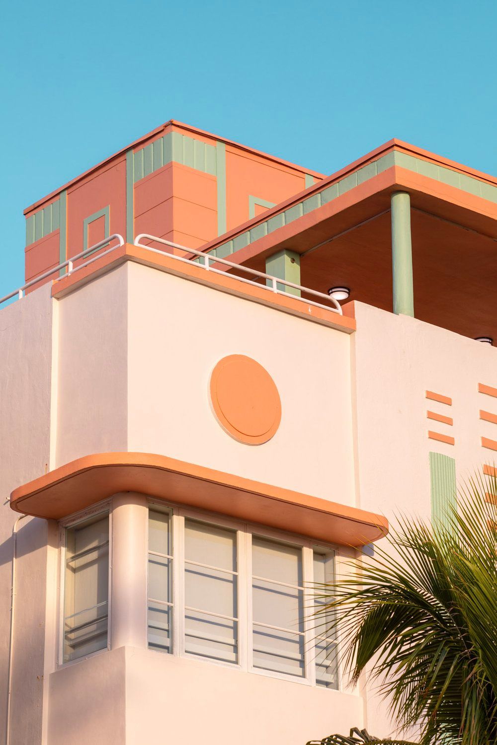 Art deco style building facade in coral and white with geometric details against blue sky.