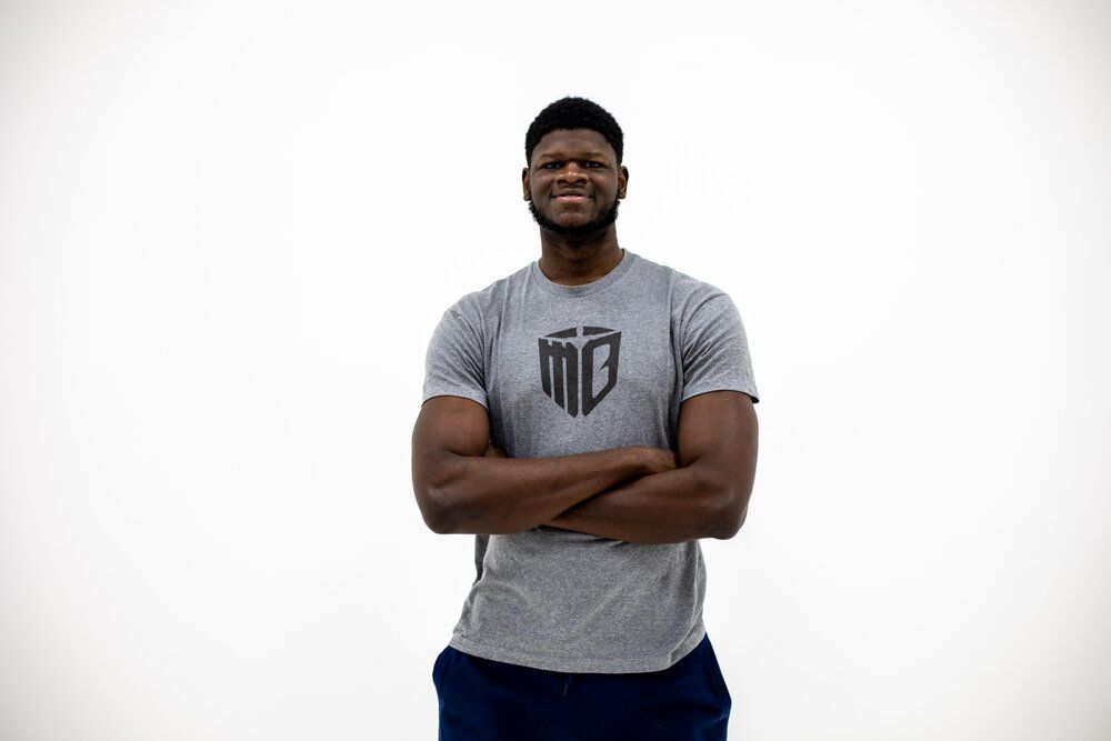 Athletic person wearing a gray t-shirt with logo stands confidently with arms crossed against white background.