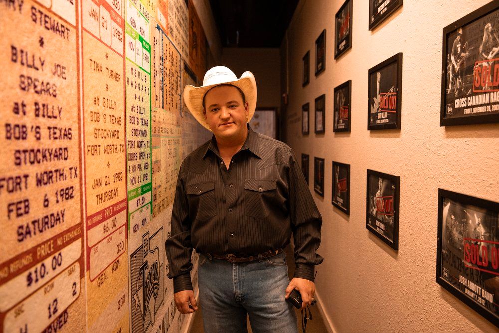 Person in cowboy hat standing in hallway with performance schedules posted on wall.