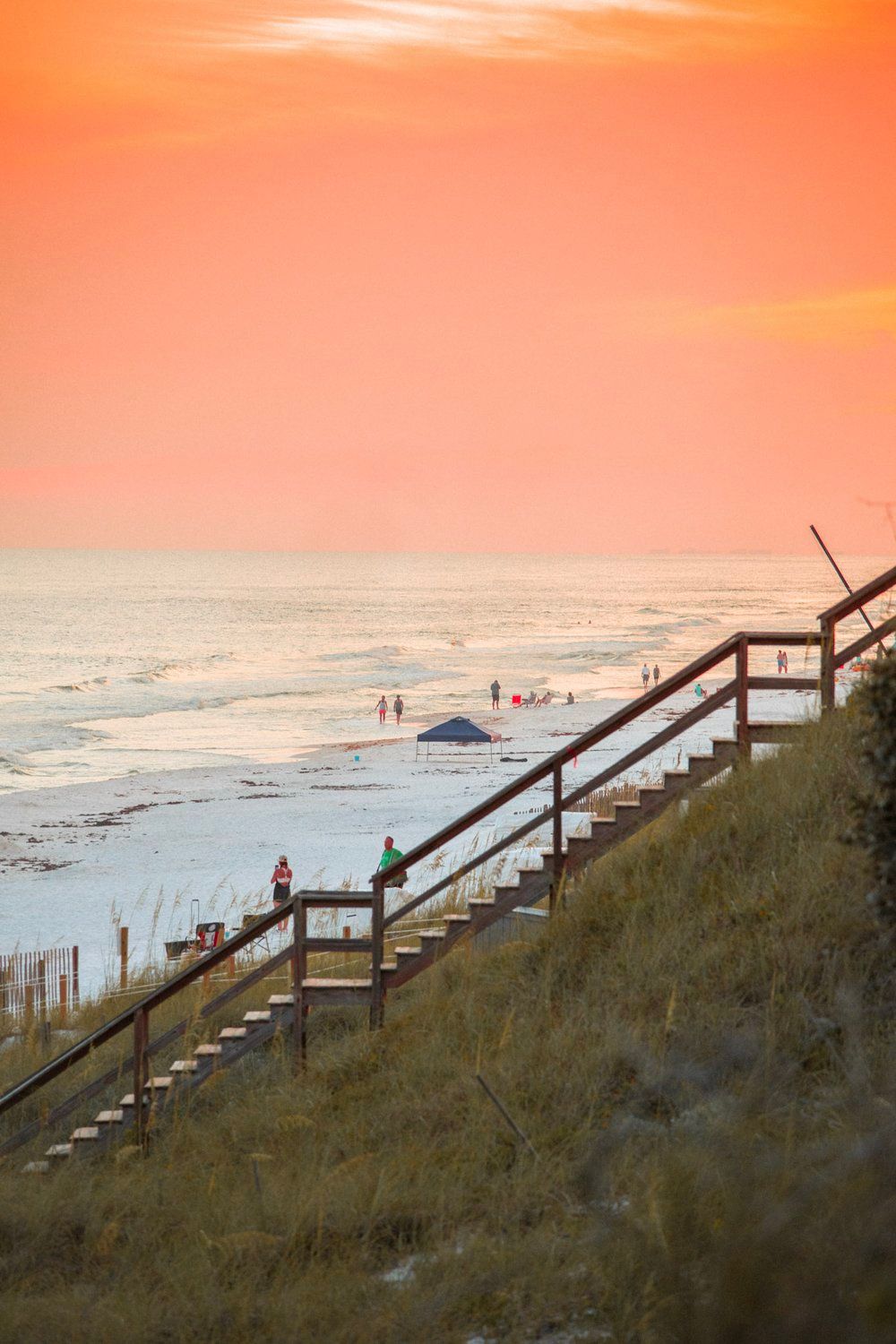 Wooden staircase leading to beach at sunset with people in the distance enjoying the waves.