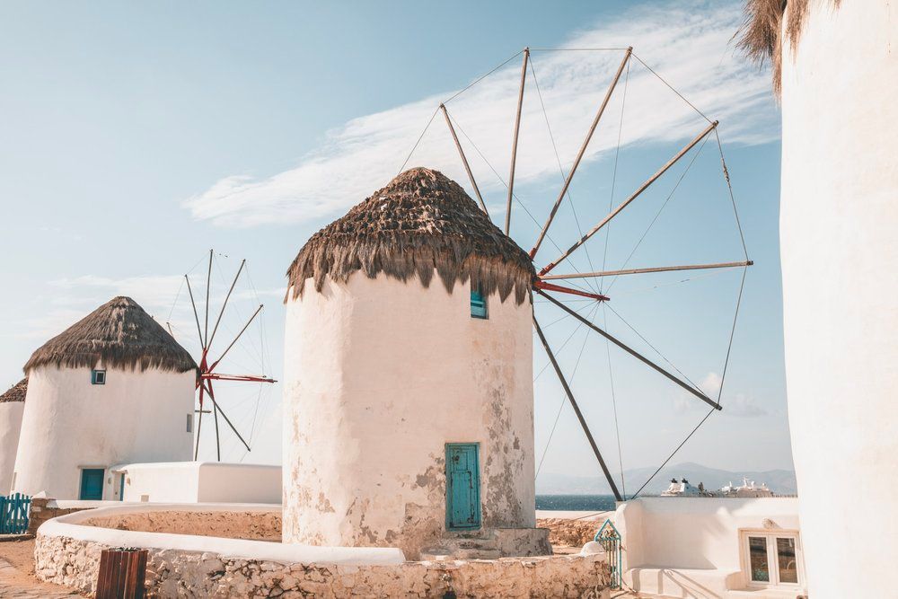 Traditional white windmills with thatched roofs against blue sky in Mykonos, Greece.