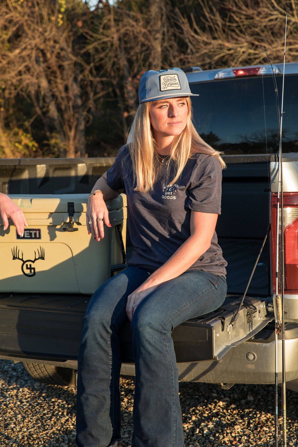 Person in baseball cap and navy t-shirt sits on the edge of a truck bed at golden hour.