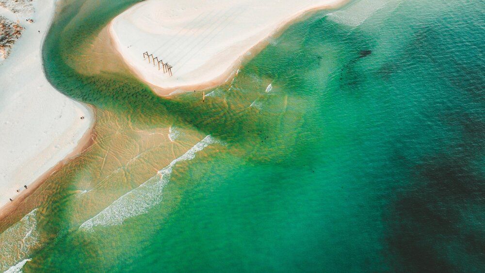 Emerald green waters meet sandy shore in a stunning aerial coastal landscape.