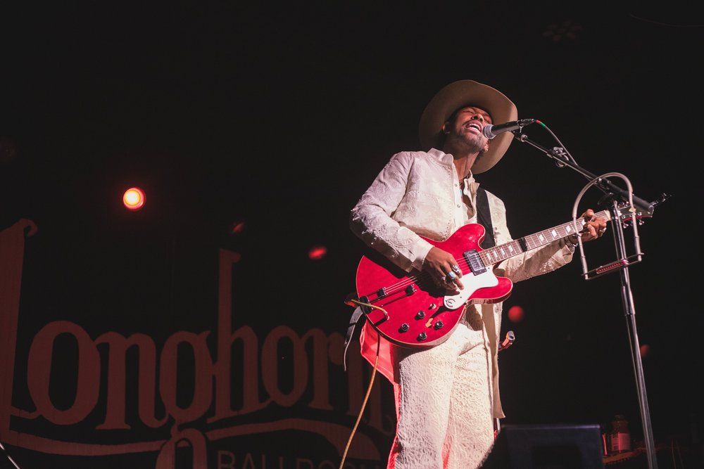 Musician in white outfit plays red guitar on stage at Longhorn venue.
