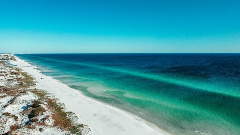 Aerial view of pristine white sand beach meeting turquoise waters along Florida's emerald coast on a clear sunny day.