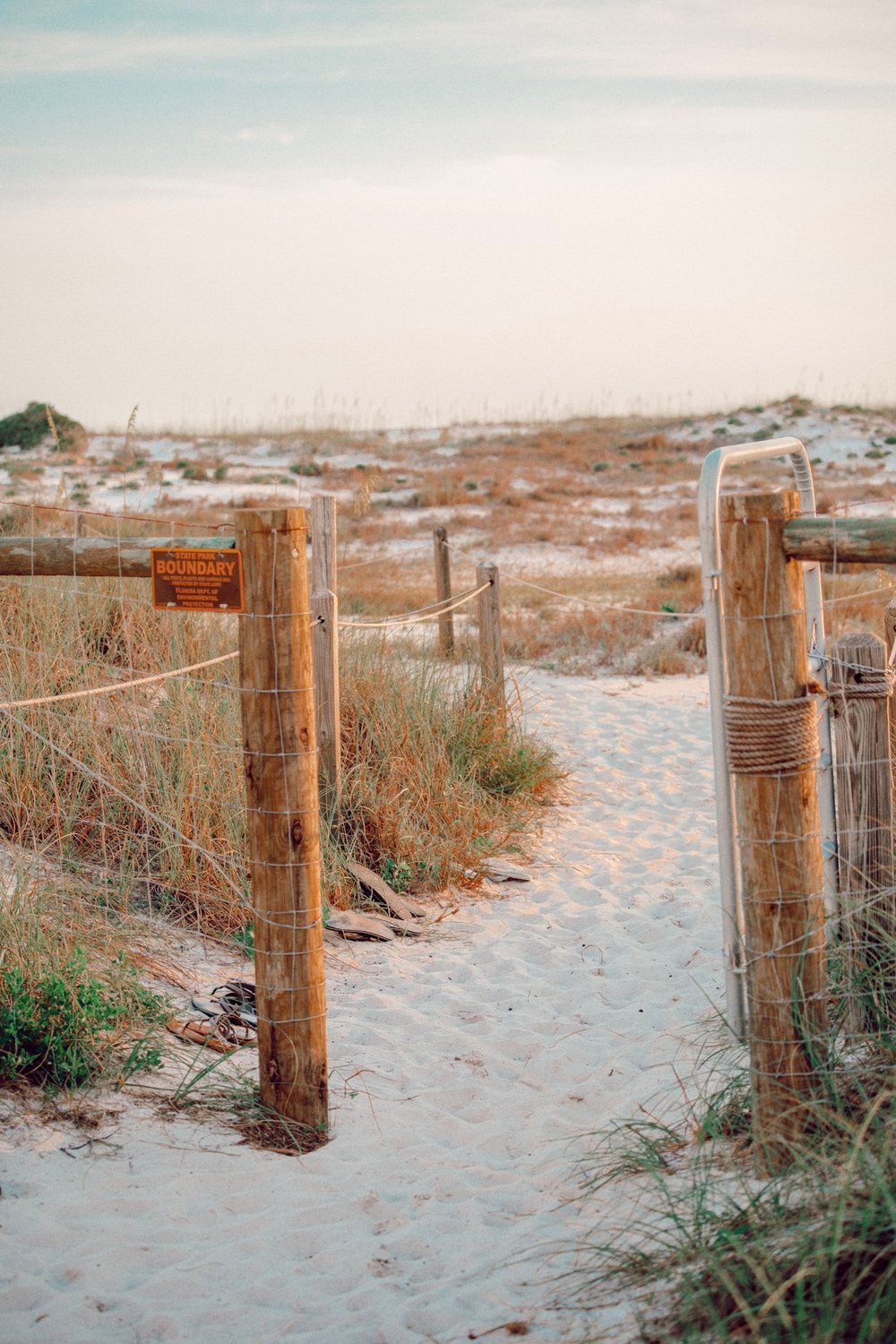 Sandy beach path between wooden fence posts leading towards the ocean.