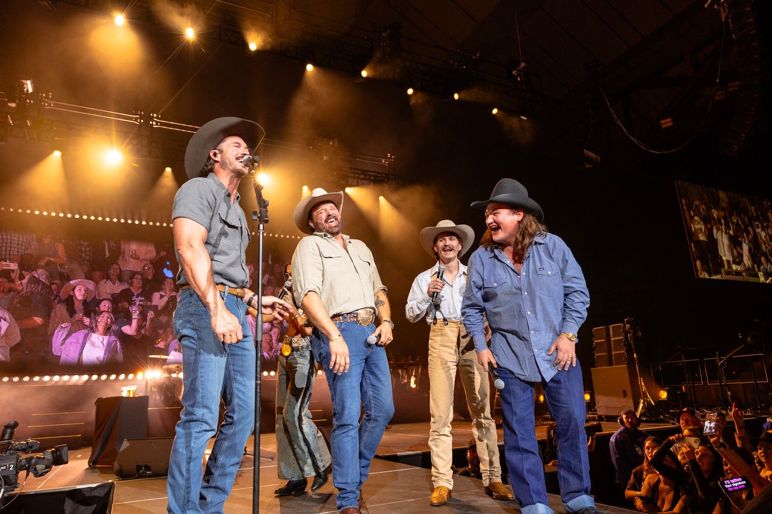 Four men in cowboy hats and jeans perform on a concert stage under dramatic lighting.