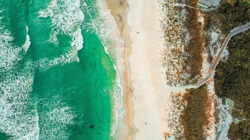 Aerial view of coastline with turquoise waters meeting sandy beach and winding coastal road.