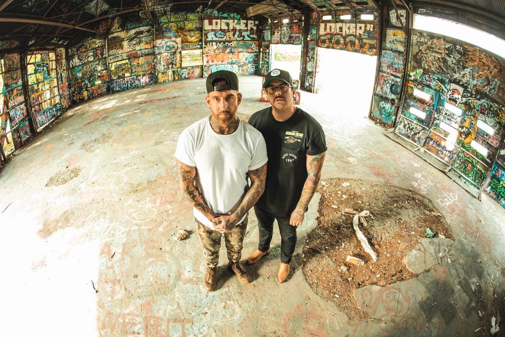 Two casual figures stand in curved graffiti-covered space with fisheye lens perspective.