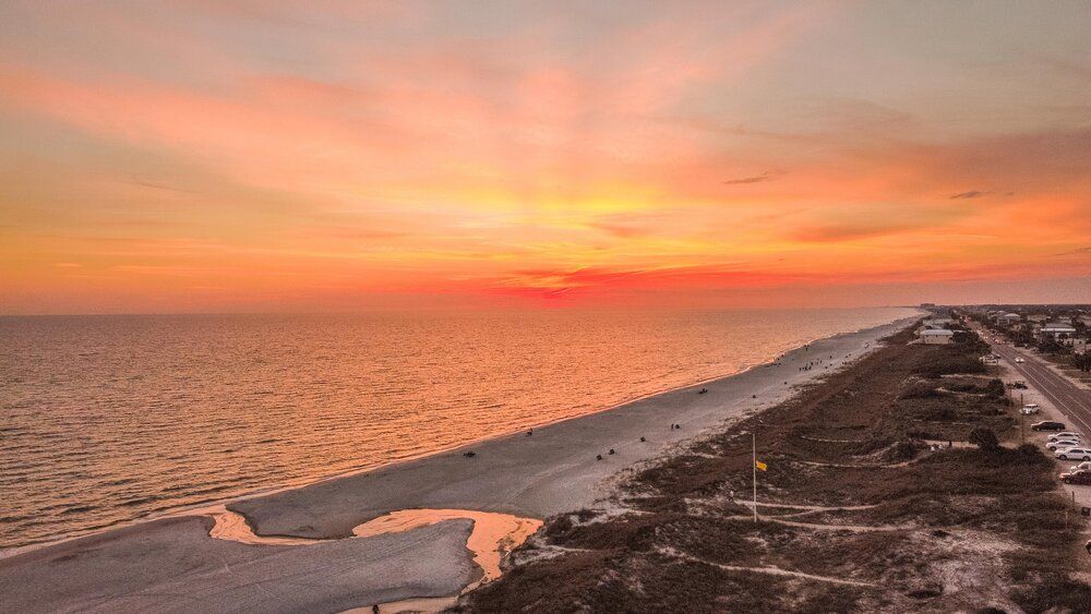 Orange and pink sunset over beach coastline with snow patches visible on sand.