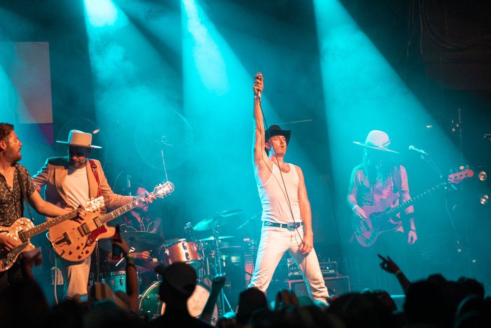 Rock band performs on stage with dramatic turquoise lighting and enthusiastic crowd.