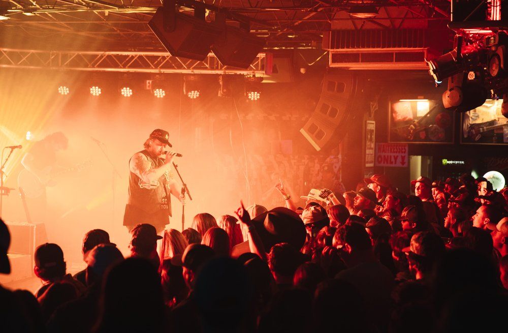 Concert crowd watches performer on stage through atmospheric red lighting and smoke effects.