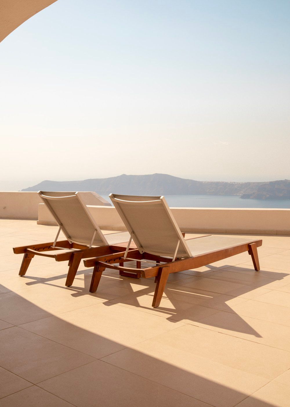 Two lounge chairs on a terrace overlooking coastal mountains and ocean views.