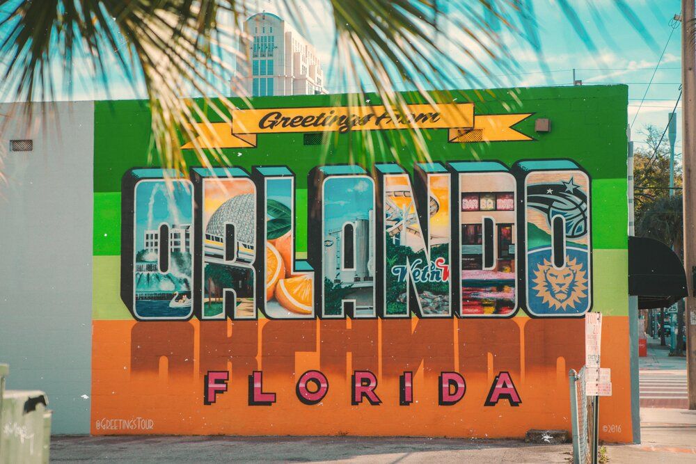 Colorful vintage-style Orlando Florida mural painted on wall with tropical palm fronds in foreground against blue sky.