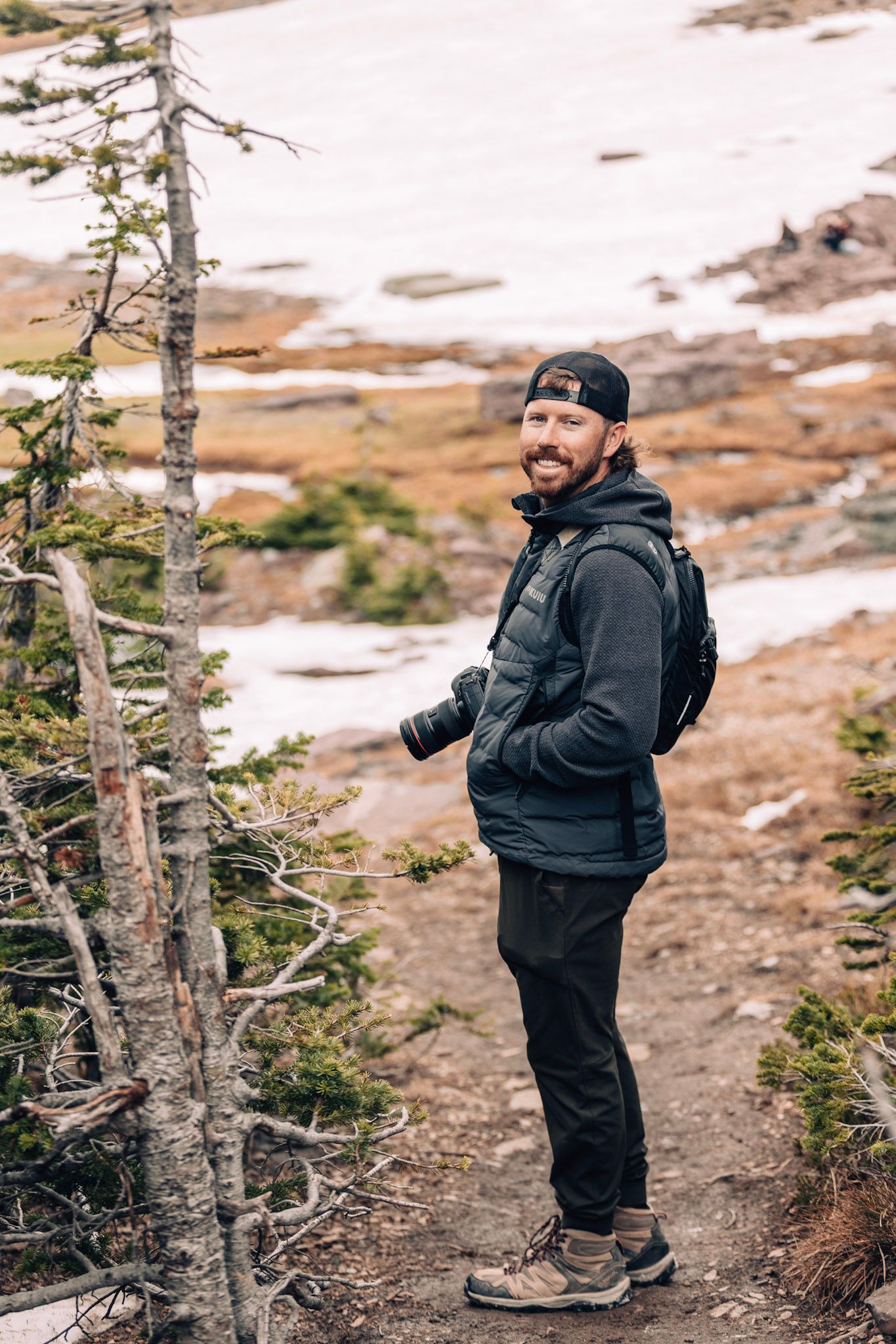 A person in warm outdoor gear explores a snowy mountain trail path surrounded by evergreen trees.