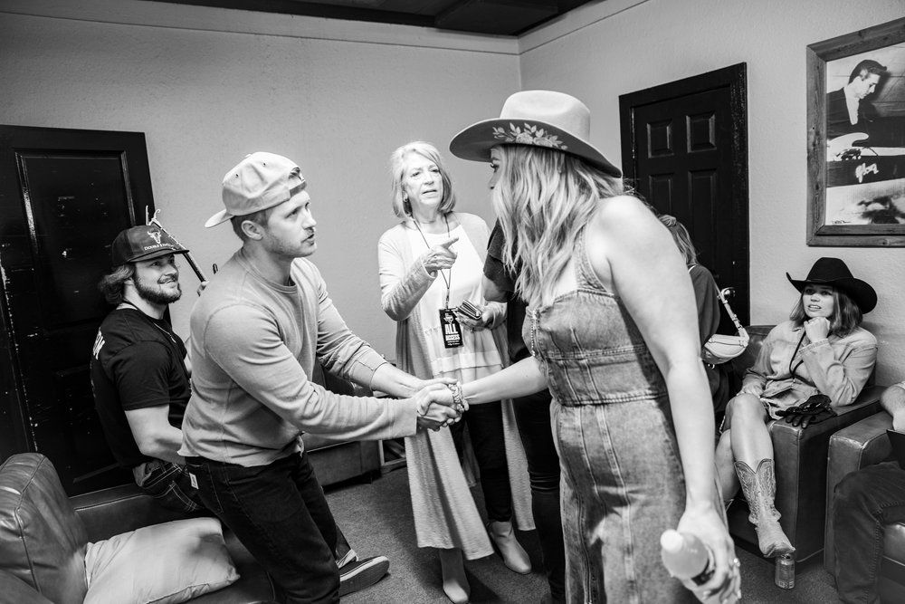 People gathered in a casual indoor setting with western attire exchanging greetings in black and white photography.