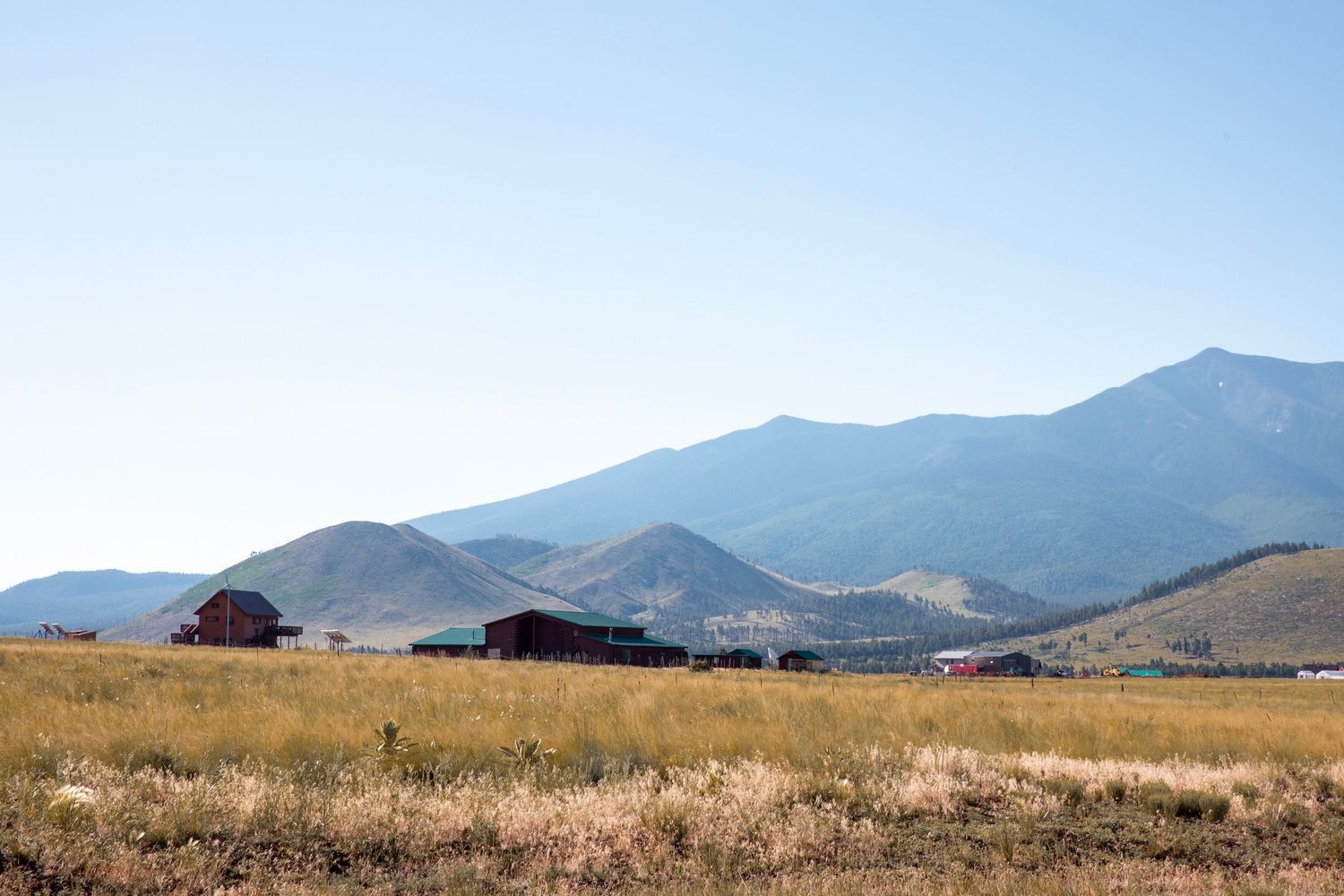 Rural mountain landscape with rustic buildings nestled against rolling hills and distant peaks.