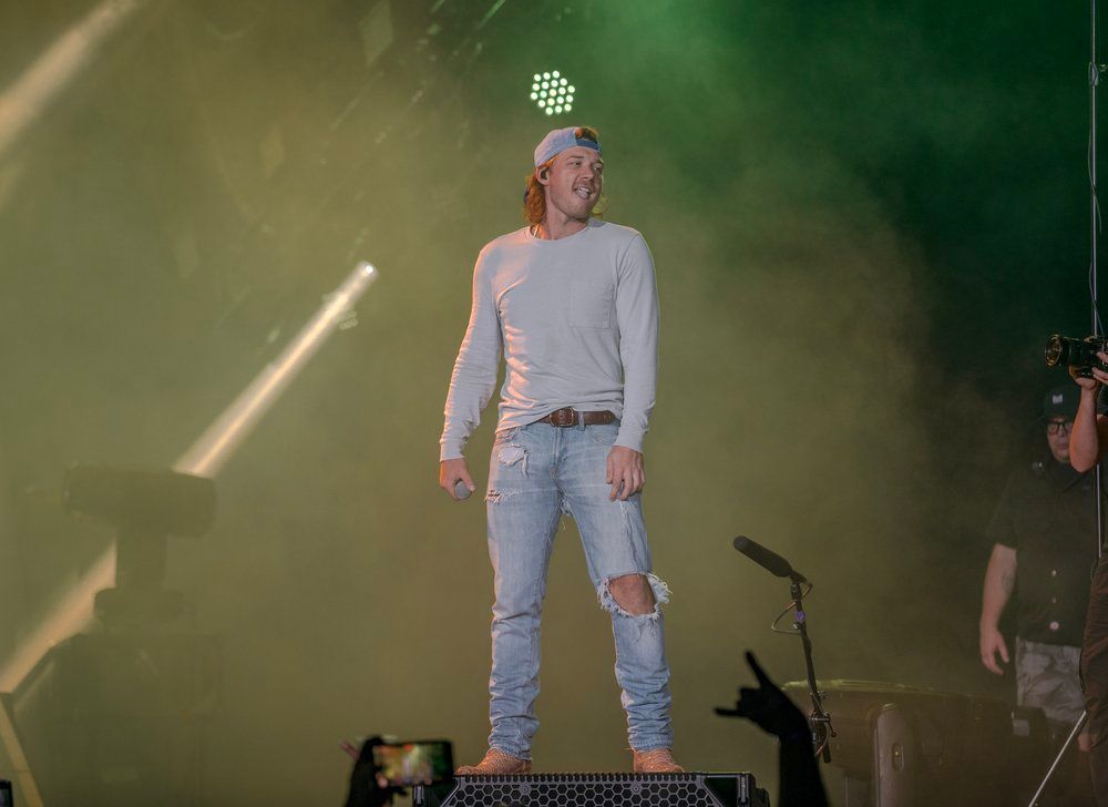 Performer Morgan Wallen in light colored outfit standing on stage with green lighting effects.