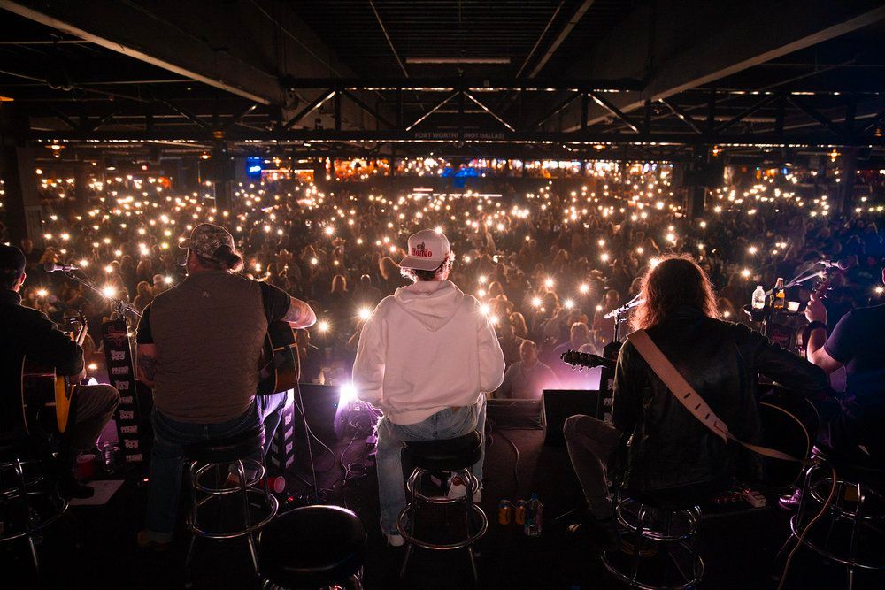 Concert crowd holds up glowing phone lights creating a sea of illumination during performance.