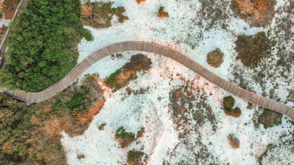 Aerial view of a winding boardwalk path through white sand and shallow waters.