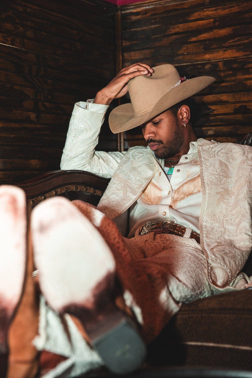 A person in western attire and cowboy hat reclines in a rustic wooden interior.