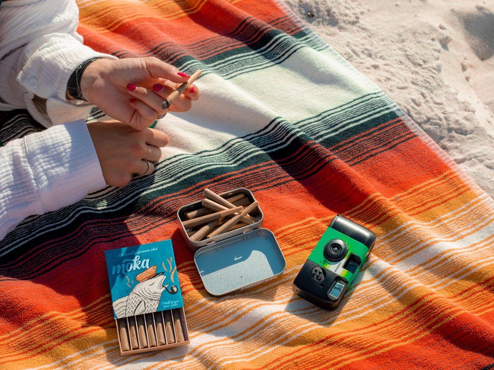 Beach essentials including a colorful striped blanket, kalimba musical instrument, disposable camera, and hand sanitizer on sand.