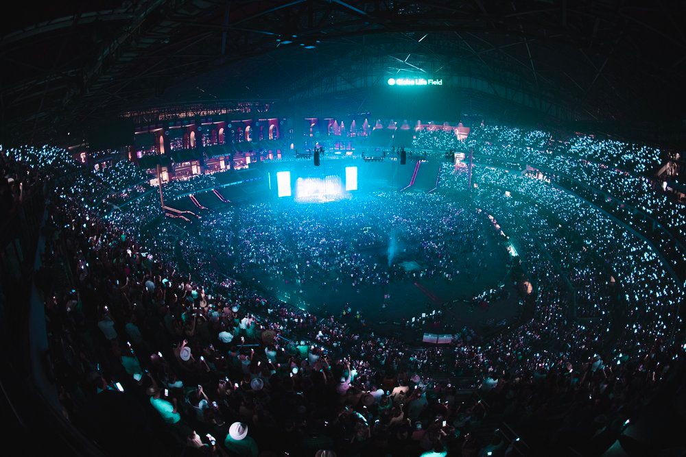 Massive arena concert venue filled with glowing cellphone lights during a nighttime performance.