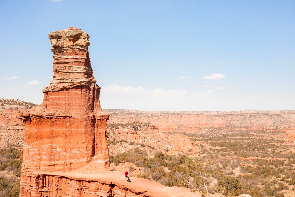 Towering red rock formation stands against clear blue sky in desert landscape.