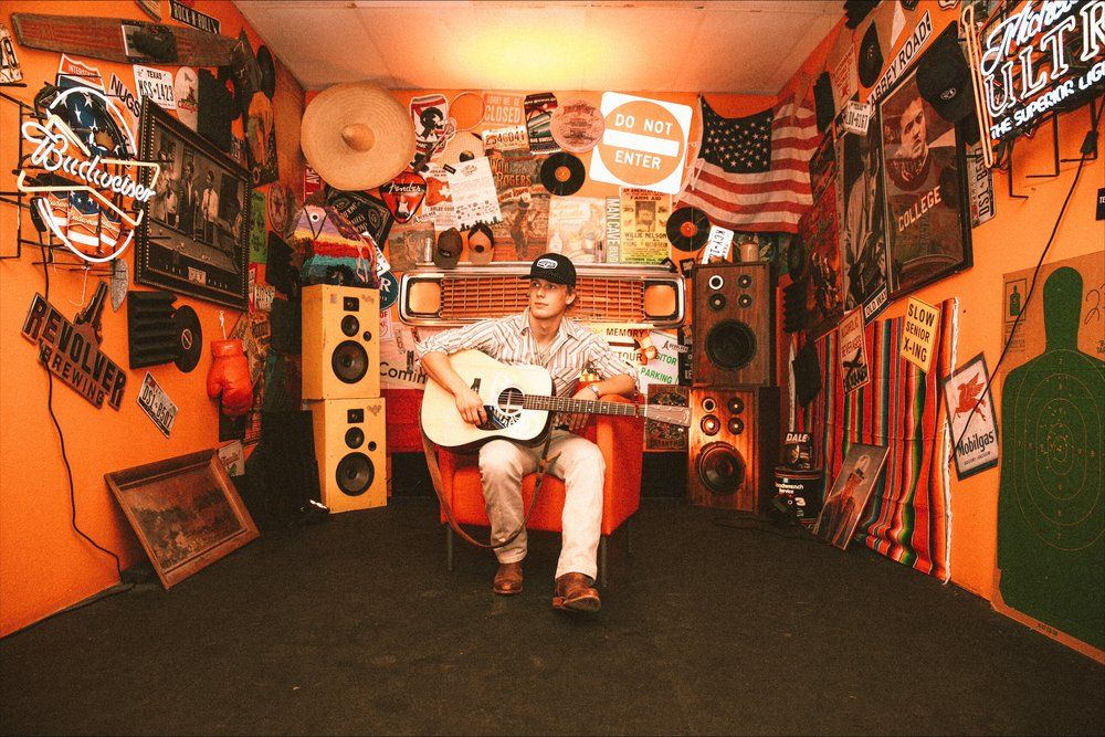 Musician performing with acoustic guitar in room decorated with vintage memorabilia and neon lights.