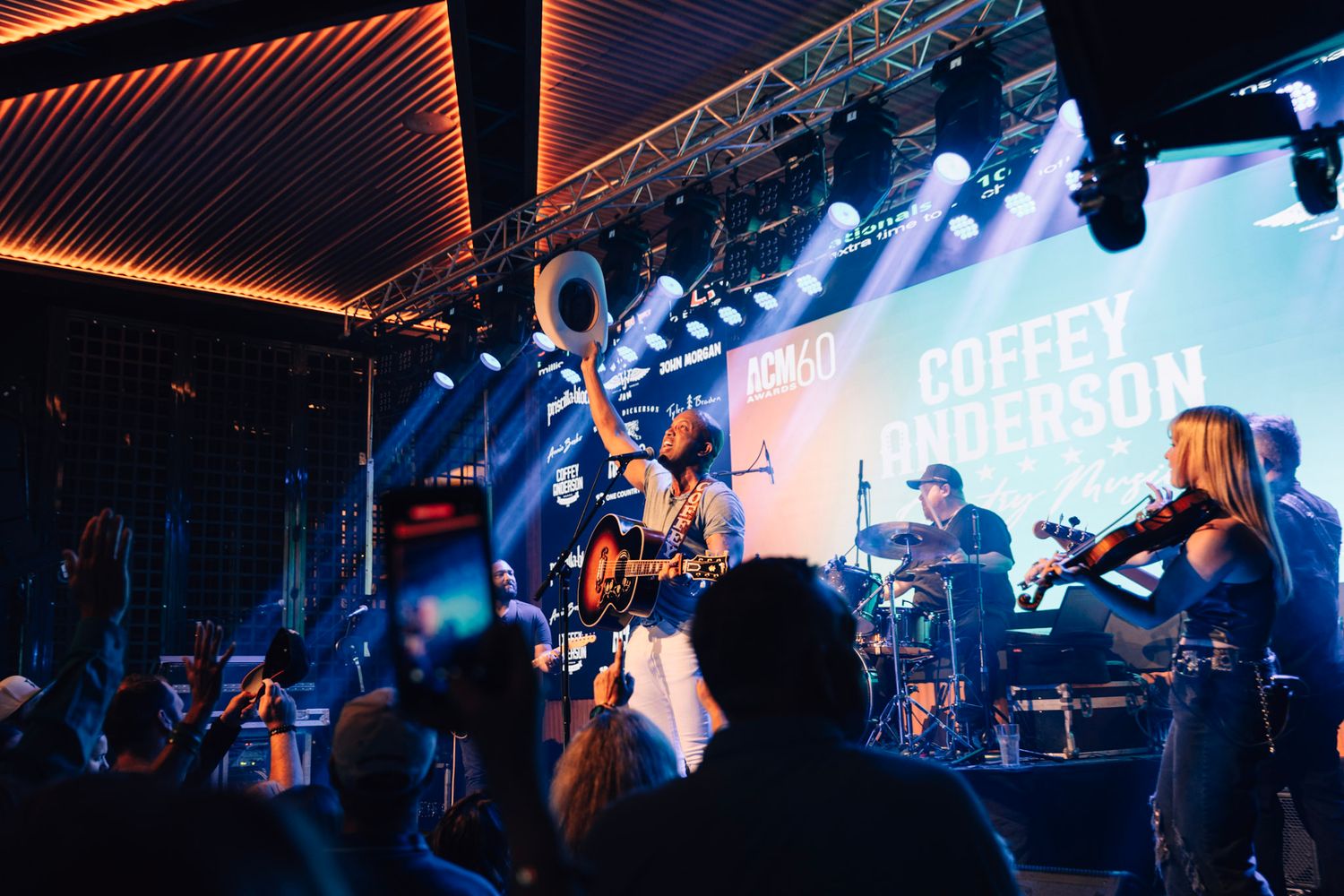 Live concert performance with band on stage under blue lighting and orange ambient glow at a music venue.