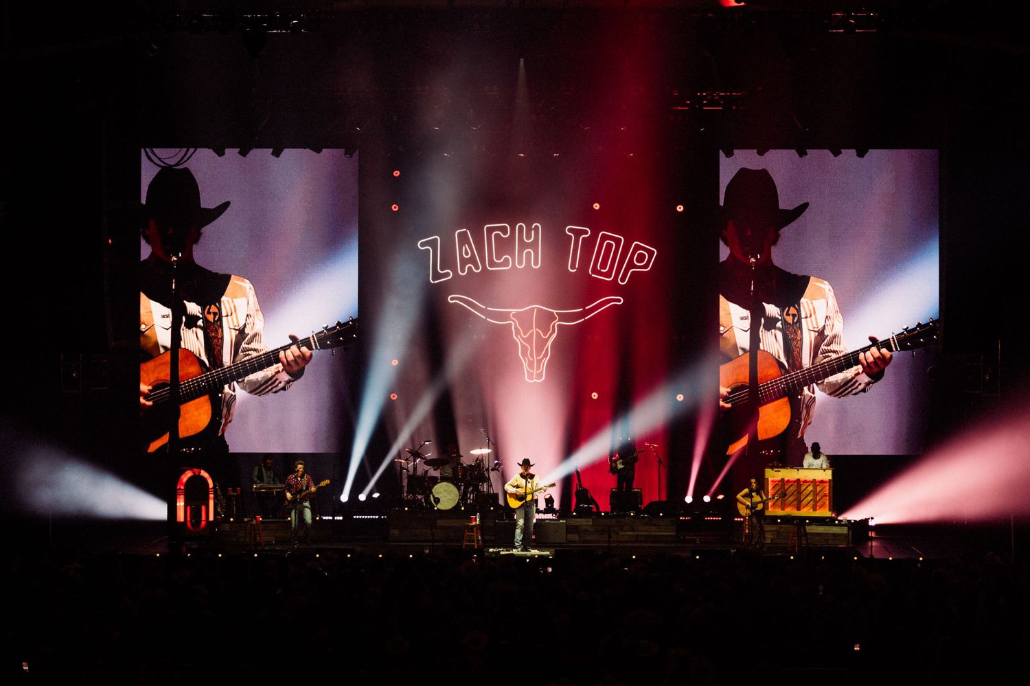 Concert stage illuminated with dramatic red lighting and silhouettes of performers and instruments.