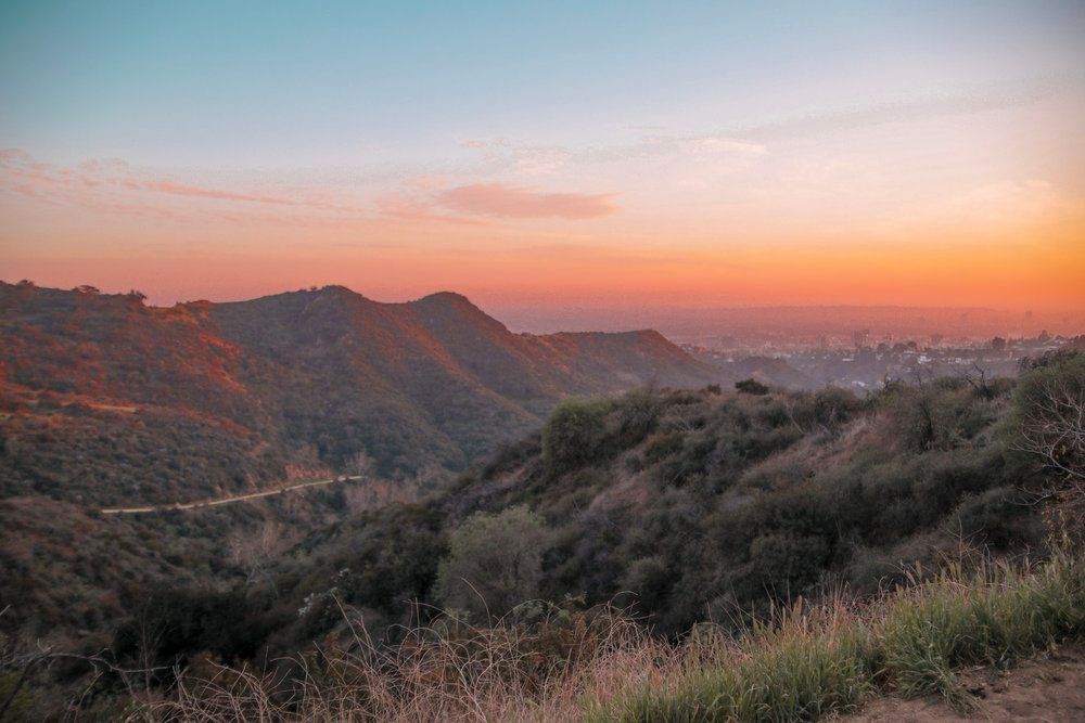 Sunset over mountain landscape with pink and orange sky illuminating rugged terrain.