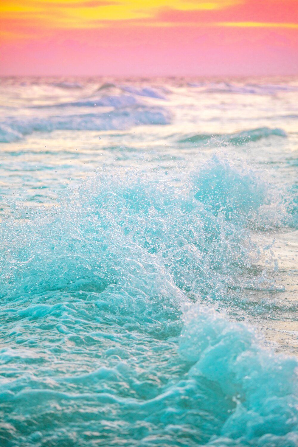 Turquoise ocean waves in Rosemary Beach, Florida crash under a vibrant pink and orange sunset sky creating a dreamy tropical seascape.