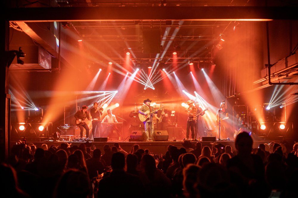 Large concert crowd watches performers on stage with dramatic red lighting and special effects.